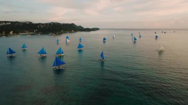 Geleneksel mavi yelkenli yelkenliler geniş bir tropikal denizde pastel renkli gökyüzünün altında yüzerler. Boracay Adası, Filipinler.