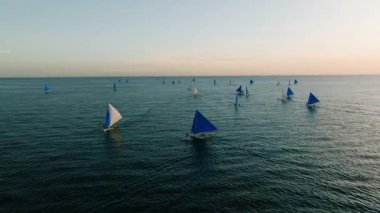 Sıcak bir günbatımı, sakin denizde huzur içinde yüzen yelkenlileri aydınlatırken gökyüzünü ve okyanusu aydınlatır. Boracay Adası, Filipinler.