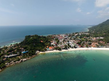 Sahil şeridi boyunca yeşil tepeler ve turkuaz sular arasında canlı bir köy kurulmuştur. Haad Rin. Ko Pha Ngan, Tayland.