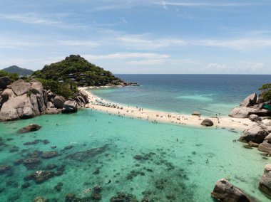 Açık gökyüzünün altında turkuaz sularla ve tropikal manzarayla çevrili iki alanı birbirine bağlayan kum çubuğu. Tayland, Koh Tao.