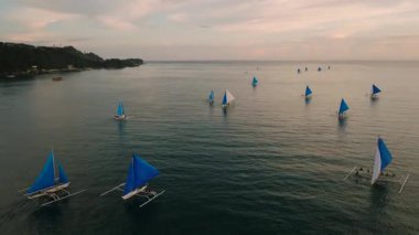 Mavi, günbatımında sakin sularda yüzen tropikal tekneler ufuktaki altın renkleri yansıtıyordu. Boracay Adası, Filipinler.