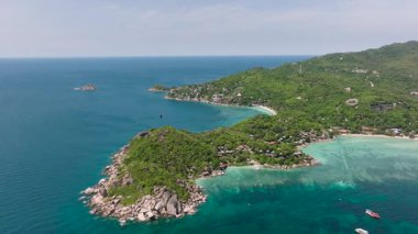 Geniş okyanus manzarası, yeşil tropikal tepeler ve parlak bir gökyüzü altında sakin sular. Koh Tao, Tayland.