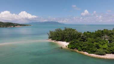 Turkuaz su, tropikal yeşillik ve parlak mavi gökyüzünün altındaki uzak tepelerin bulunduğu sakin kıyı manzarası. Cape Fahn 'da. Koh Samui, Tayland.