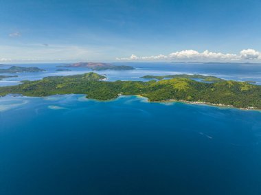 Kıyılarında küçük bir köy olan tropikal adanın çarpıcı manzarası mavi deniz yüzeyi, mavi gökyüzü ve bulutlar. Deniz Burnu. Mindanao, Filipinler.
