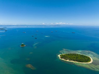 Adadaki kumsalda mavi deniz ve mercan resifleri var. Mavi gökyüzünün altında okyanusta tekneler. Mindanao, Filipinler.