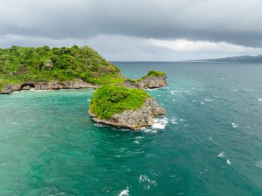 Güzel deniz dalgaları bulutlu gökyüzünün altında kayalara ve adacıklara çarpıyor. Boracay, Filipinler.