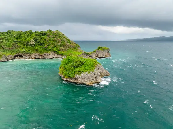 Güzel deniz dalgaları bulutlu gökyüzünün altında kayalara ve adacıklara çarpıyor. Boracay, Filipinler.