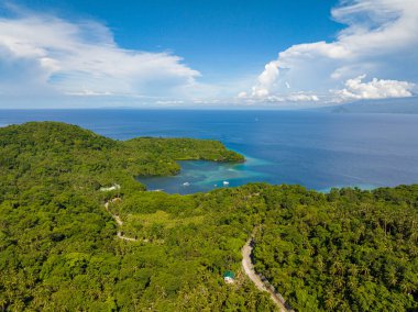 Camiguin Adası 'nın sahil şeridi üzerinde orman ve yol bulunan tropik bir manzara. Mavi deniz, mavi gökyüzü ve bulutlar. Filipinler.