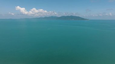 Ufuk çizgisine kadar uzanan durgun turkuaz deniz yeşil dağlar ve arka planda açık mavi bir gökyüzü. Koh Pangan, Tayland.