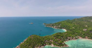 Bereketli yeşillikler ve mavi gökyüzünün altındaki dağınık kulübelerle çevrili sakin turkuaz su. Koh Tao, Tayland.