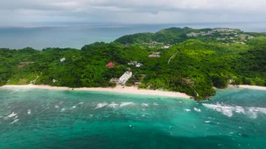 Bereketli yeşil tepeler dağınık binalarla el değmemiş bir sahil şeridi boyunca turkuaz okyanusla buluşuyor. Ilig Iligan Sahili. Boracay Adası, Filipinler.