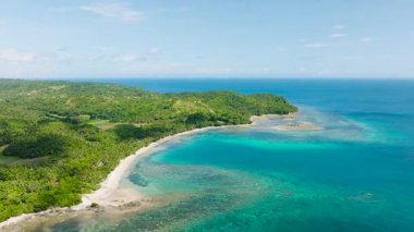 Geniş bir sahil şeridi. Canlı yeşil bitki örtüsü ve parlak bir gökyüzü altında masmavi bir suya çarpıyor. Santa Fe, Tablo, Romblon, Filipinler.