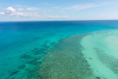 Deniz yüzeyi mercanlar ve turkuaz berrak sularla kaplı tropikal deniz manzarası. Mavi gökyüzü ve bulutlar. Bantayan, Cebu, Filipinler.