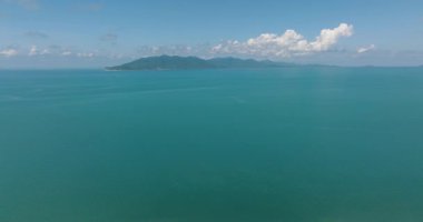 Ufuk çizgisine kadar uzanan durgun turkuaz deniz yeşil dağlar ve arka planda açık mavi bir gökyüzü. Koh Pangan, Tayland.