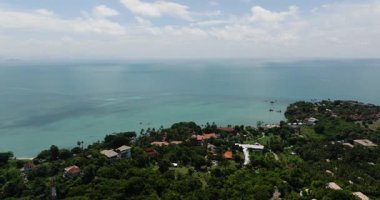 Berrak bir gökyüzü altında yemyeşil bitki örtüsü ve sakin turkuaz sularla çevrili deniz kenarı köyü. Ko Samui, Tayland.