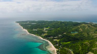 Kıyı manzaralı yeşil tepeler, turkuaz sular ve parçalı bulutlu bir gökyüzünün altında kumlu plajlar. Santa Fe, Tablo, Romblon, Filipinler.