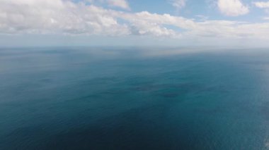 Bulutlu bir gökyüzünün altında ufka uzanan sakin mavi okyanusun geniş bir görüntüsü. Santa Fe, Tablo, Romblon, Filipinler.