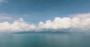 Sakin turkuaz okyanus, uzak yeşil adalar ve parlak mavi gökyüzü ile dramatik bulutlar geniş bir görünüm. Ko Pha Ngan, Tayland.
