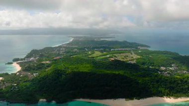 Bereketli yeşil tepeler ve kumlu bir kıyı şeridi bulutlu bir gökyüzünün altında turkuaz sularla birleşiyor. Boracay Adası, Filipinler.