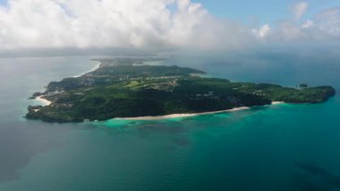 Yuvarlanan yeşil tepeler bulutlu ama parlak bir gökyüzünün altında kumlu kıyı şeridi ve turkuaz sularla buluşuyor. Boracay Adası, Filipinler.