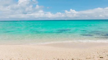 Açık turkuaz sularda hafif dalgalar parlak bir gökyüzünün altında kumlu bir kıyıya çarpıyor. Puka Kabuğu, Boracay Adası, Filipinler.