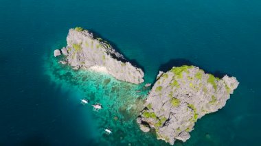 Mavi deniz ve mercanlarla çevrili kıyılarda tekneleri olan küçük adaları gösteren manzara. Miniloc Adası. El Nido, Filipinler.