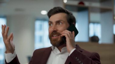 Akıllı telefondan konuşan mutlu bir işçi. Yakın plan. Memnun ofis çalışanı gülümseyerek cep telefonundan iyi haberleri tartışıyor. Başarılı bir şirket ortamında olumlu bir jest. Patron başarının tadını çıkar