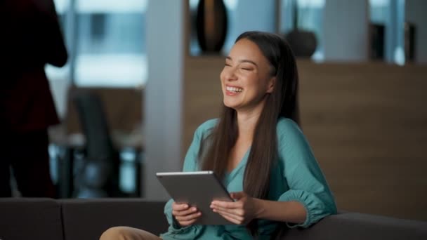 オフィスのロビーでタブレットを見て幸せなビジネス女性が閉じます 面白い感情を持つデジタルコンピュータを使用して陽気な起業家 興奮エグゼクティブスクロール技術デバイスアプリケーション休息ソファだけ — ストック動画