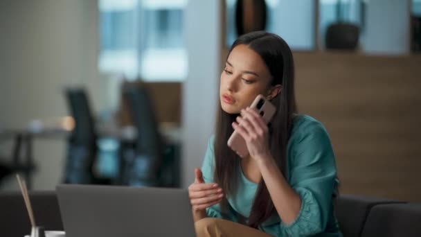 ソファのクローズアップで忙しい開発者が電話に答える Brunetteのプロジェクトマネージャーは ビジネスパートナーと電話で会話するラップトップを見ています オフィスでスマートフォンを話す成功したビジネス女性 — ストック動画