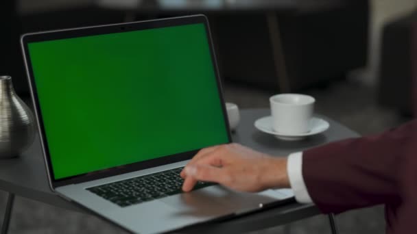 オフィスのクローズアップにモックアップコンピュータを入力して不明監督 男は屋内で緑の画面デバイスを動作武器 匿名の起業家は ワイヤレス近代的なガジェットを使用してクロマキーノートパソコンの向かいに座って — ストック動画