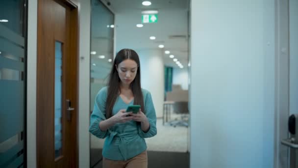 亚洲女商人在办公室用手机发短信 专业女歌手在走廊里用智能手机浏览互联网 重点经理步行玻璃走廊 企业忙碌的生活方式概念 — 图库视频影像
