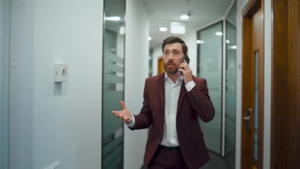 ビジネスセンターで携帯電話を議論する感情的な男 ガラスの壁の廊下で議論のスマートフォンを保持する神経質なビジネスマン オフィスの廊下で叫んで怒っている専門家の散歩を閉じます — ストック動画