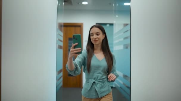 幸せなプロジェクトマネージャーのビデオを離れて廊下を歩いて呼び出します 携帯電話の挨拶の手を握るスマートなビジネス女性 ガラスの壁の廊下に沿って仮想会話をしている自信のある従業員 — ストック動画