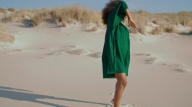 Siyah elbiseli, kum çölünde çağdaş bir dansçı kadın. Afrika kökenli, enerjik bir kız yaz günü kum tepelerinde duygusal olarak dans ediyor. Kıvırcık esmer, doğa performansının keyfini çıkar..
