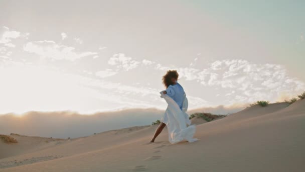 有才华的年轻姑娘在落日的天空中 在沙漠中 与飘扬的白布共舞 卷曲的非洲裔美国女人优雅地举着轻薄的布 吹着夏日的寒风 舞蹈概念 — 图库视频影像