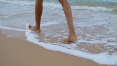 Okyanus sahilinde yürüyen bacaklar. Sıska kadın ayakları tek başına su sıçratıyor. Tanınmayan romantik Afrikalı Amerikalı turist kumsal tatilinin tadını çıkarıyor. Yaz zamanı cennet konsepti.