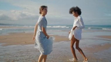 Yaz tatilinde sahilde dans eden mutlu kızlar. Heyecanlı gülümseyen Igbt çifti birlikte okyanus kıyısında tatilin tadını çıkarın. Çok ırklı enerjik kadın partnerler tatilde eğleniyorlar. Aşk mutluluk kavramı