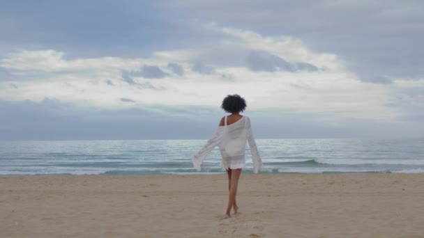 无忧无虑的女孩跑到海滩后视镜 快乐性感的女人穿着白色比基尼享受着和平的沙滩海岸线 身份不明的非洲裔美国游客在平静的海浪中悠闲自在地散步 感觉良好的概念 — 图库视频影像