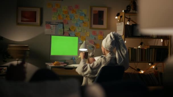 無名の少女がコンピュータのクローズアップを休んでいる 主婦がリモートで働いてお茶を飲むのを見る シャワー後に緑色の画面を見て匿名のバスローブの女性 居心地の良い家で学ぶ学生 — ストック動画