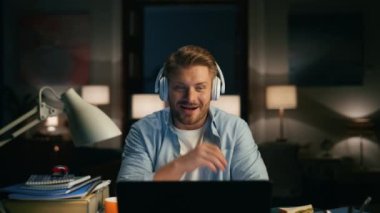 Neşeli blogcu karanlık dairelerde web kamerasından bahsediyor. Mutlu adam gece tek başına video görüşmesi yapıyor. Pozitif kulaklıklı adam, evdeki rahat bir akşamda video konferansında el sallıyor.