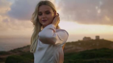 Romantik model akşam zum yaparken doğayı rahatlatıyor. Sonbahar ortamında el kamerasını esneten olumlu bir kadın. Sarışın kız saçlarına dokunuyor rüzgarlı havalarda okyanus arka planında dinleniyor.