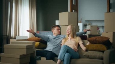 Mutlu çift rahat koltukta oturarak yeni evine taşınmayı seviyor. Genç heyecanlı aile kucaklaşması dolu kutularla dolu modern kiralık bir daireye taşınma sevinci. Evli çift mutluluğu hisseder.