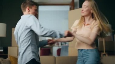 Genç ve komik çift, paketlenmiş kutularla dolu yeni bir dairede dans ediyorlar. Mutlu aile, modern ev almaktan memnun. Birlikte eğlenin. Neşeli ev sahipleri oturma odasında oynaşıyor..