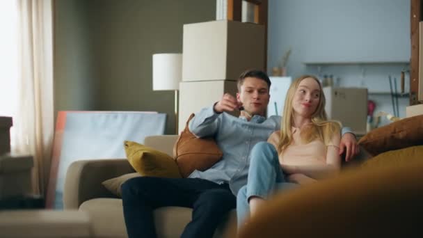 一个快乐的男人把钥匙给了一个金发漂亮的女人 她坐在拥挤的箱子旁舒服的沙发上 快乐的年轻夫妇笑着享受搬到现代买房的乐趣 — 图库视频影像