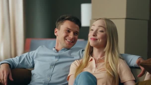 兴奋地微笑着的家人坐在客厅沙发上的新公寓里放松一下 年轻夫妇计划一起讨论家具的内部装修 搬进新房子的可爱的配偶 — 图库视频影像