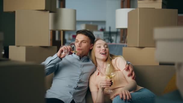 幸福可爱的夫妇庆祝购买新的房子坐在客厅与高脚杯特写 年轻的家庭在纸盒间悠闲自在地喝酒 满意的男人喜欢住在公寓里 — 图库视频影像