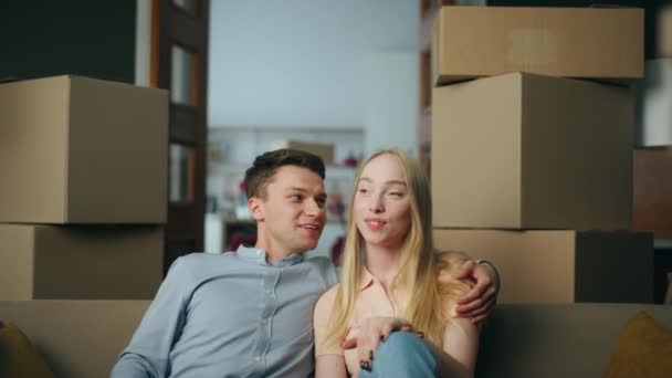 一对积极的年轻夫妇坐在舒适的沙发上 舒适地坐着 在充满纸板箱的现代客厅里 家庭幸福地放松一下 快乐的夫妻谈论着室内新公寓 — 图库视频影像