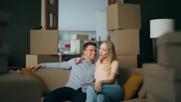 快乐的家人坐在舒适的沙发上 近距离地享受着购买的新房子 年轻满意的夫妇从打开纸盒休息一下 微笑的业主乐于购买自己的房产 — 图库视频影像