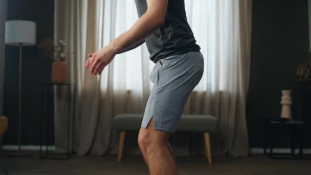 一个不知名的健美男子在密室里锻炼 穿着运动服在窗前蹲着的年轻运动员侧视图 肌肉运动员训练腿力量练习体操 — 图库视频影像