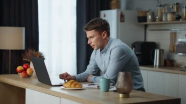 Ev mutfağında oturan iş arkadaşlarıyla zoom toplantısına odaklanmış bir adam iş süreçlerini tartışıyor. Genç işadamı video sohbet kullanarak uzaktan çalışıyor. İnternette iletişim kuran adam..